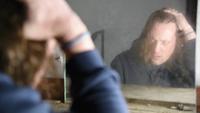 El hombre deprimido y enojado está sentado frente a su reflejo en una vieja casa abandonada