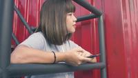 Mulher asiática nova bonita que escuta a música em um telefone esperto na cidade. Mulher asiática nova que relaxa a escuta a música na rua.