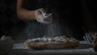 Câmera lenta das mãos de uma mulher peneirar farinha sobre uma pizza