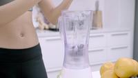 Sporty Asian woman using blender to make grape juice in the kitchen.