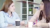 Die asiatischen Geschäftsfrauen, die genießen, warmen Kaffee zu trinken, besprechen über Arbeit.