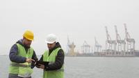 Twee havenarbeiders met helmen bekijken documenten.