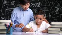 Asian teacher is helping schoolboy to write the alphabet.